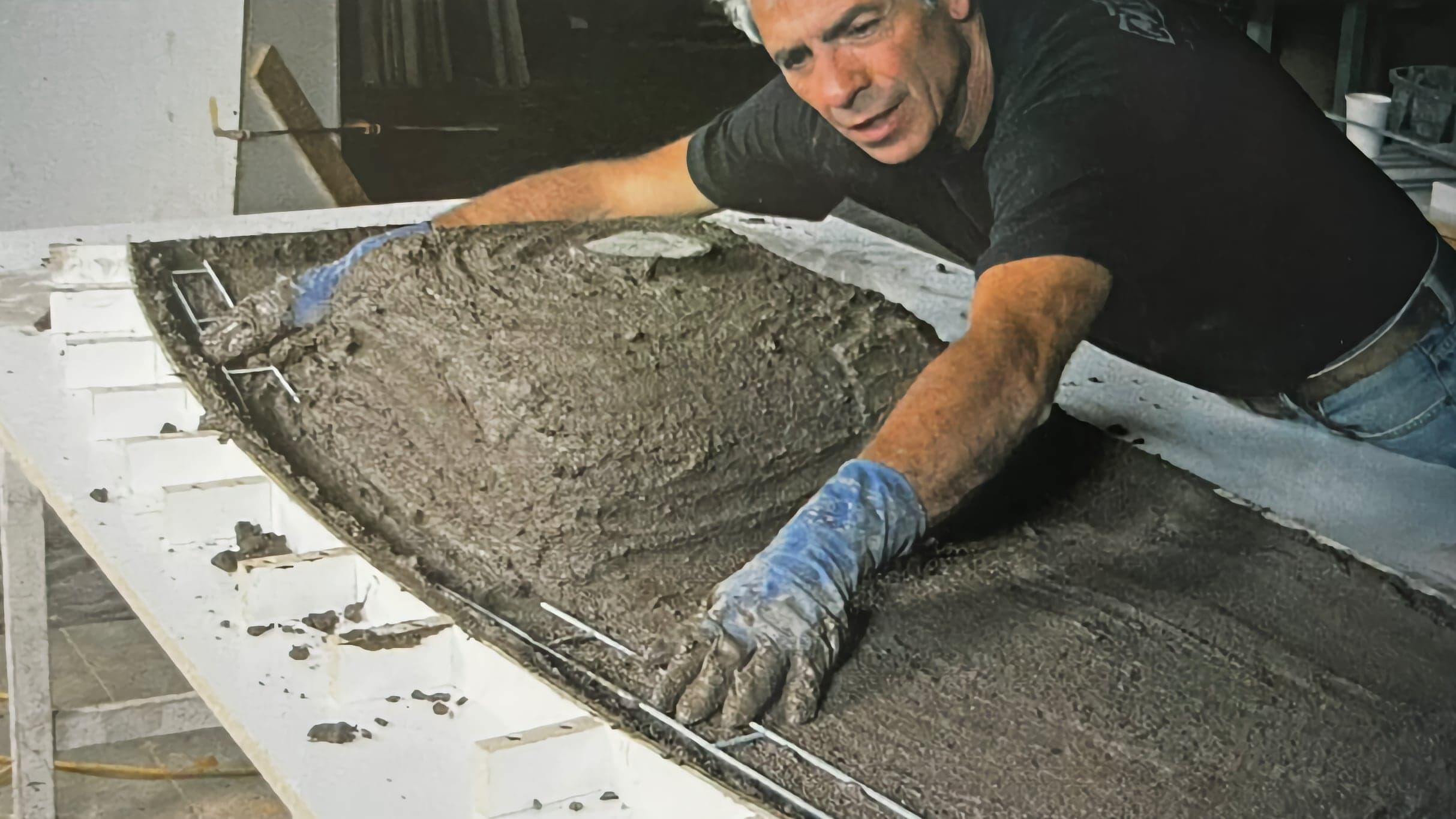 Buddy Rhodes leaning over a form, pressing fiber-reinforced concrete into a curved mold by hand